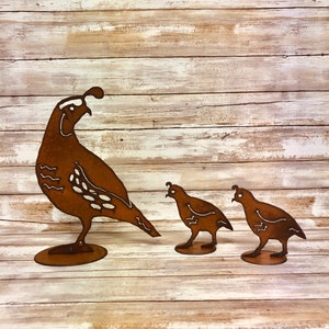 May include: A metal sculpture of a mother quail with two chicks. The quail are brown with white markings and are standing on a wooden surface.
