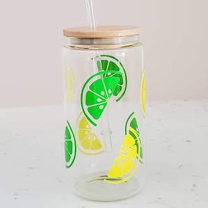 May include: A clear glass reusable water bottle with a bamboo lid and a straw. The bottle has a lemon and lime design.
