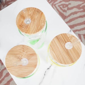 May include: Three glass tumblers with bamboo lids and clear straws. The tumblers are decorated with a yellow and green citrus design.