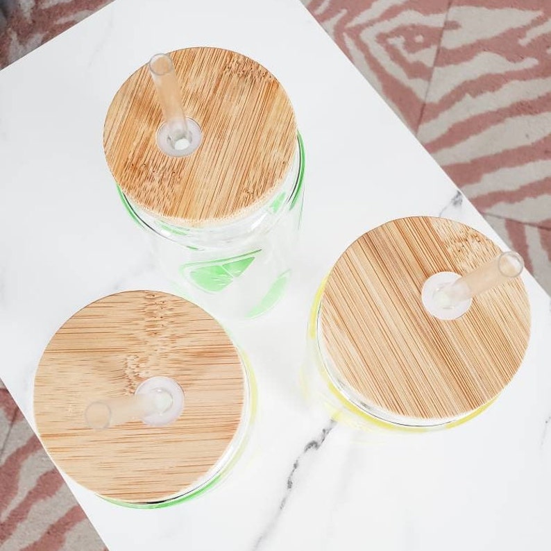 May include: Three glass tumblers with bamboo lids and clear straws. The tumblers are decorated with a yellow and green citrus design.