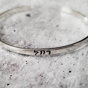 May include: A silver bangle bracelet with the Hebrew word "Chai" engraved on it.