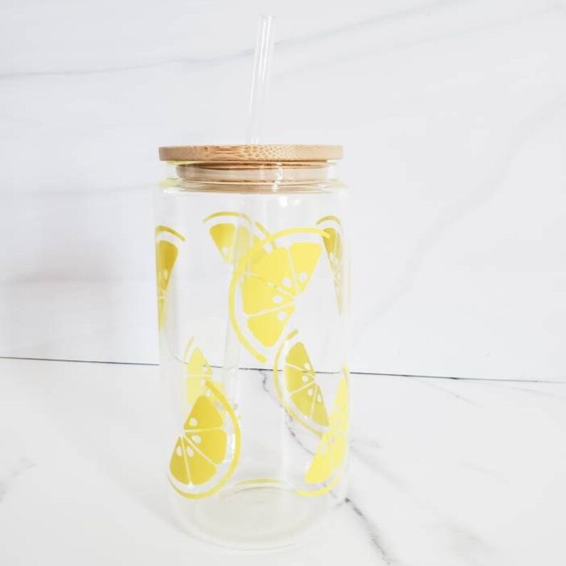 May include: A clear glass water bottle with a bamboo lid and a straw. The bottle has a yellow lemon print design.