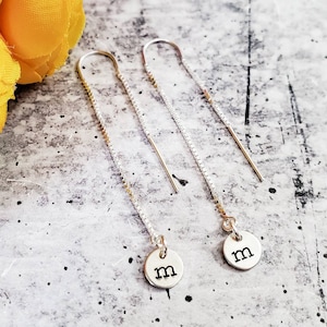 May include: A pair of silver chain earrings with a small silver disc charm with the letter 'm' on each earring.