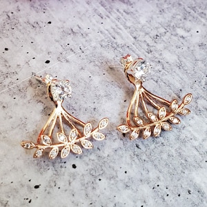 May include: A pair of gold-tone earrings with a leaf design and clear cubic zirconia stones. The earrings are designed to be worn on the upper part of the ear, with the leaves extending out and down.