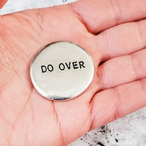 Peut inclure: Un jeton rond de couleur argent avec les mots "DO OVER" grav&eacute;s en lettres noires.