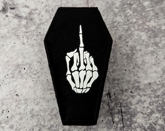 May include: A black coffin-shaped box with a white skeleton hand giving the middle finger.