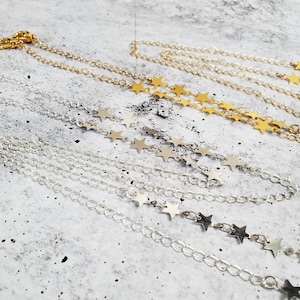 May include: Two layered necklaces with star charms. The top layer is gold and the bottom layer is silver.