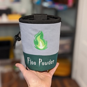 May include: A gray and green drawstring bag with a green flame design and the text "Floo Powder".