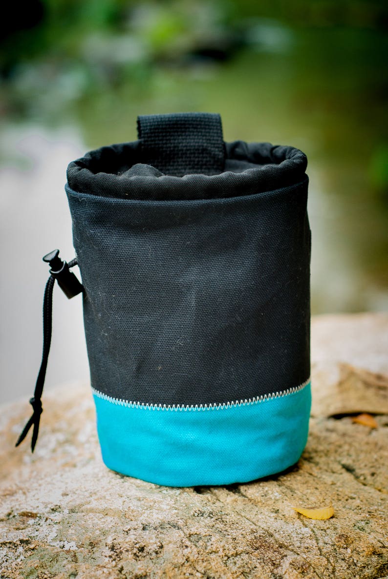 May include: A black and turquoise climbing chalk bag with a drawstring closure.