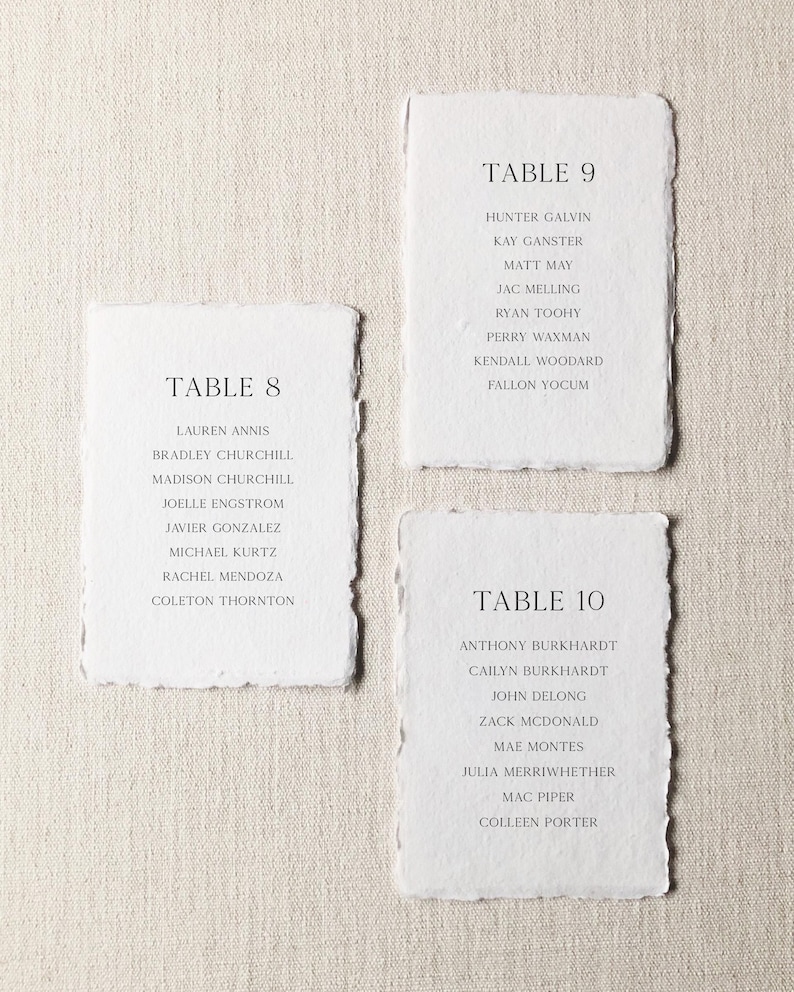 Peut inclure: Trois cartes rectangulaires en papier blanc aux bords effiloch&eacute;s, chacune avec du texte imprim&eacute; en noir. Les cartes sont intitul&eacute;es TABLE 8, TABLE 9 et TABLE 10, suivies de listes de noms incluant Lauren Annis, Hunter Galvin et Anthony Burkhardt.