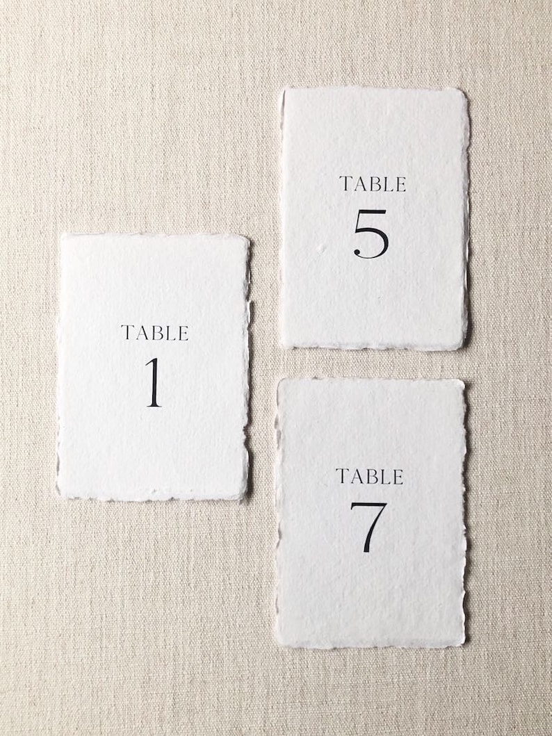 May include: Three white table number cards with black text. The cards read "Table 1", "Table 5", and "Table 7".
