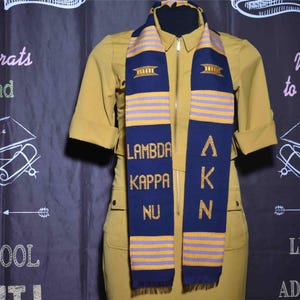 May include: A gold and purple graduation stole with the letters "AKN" and the words "Lambda Kappa Nu" embroidered on it.