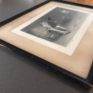 May include: A black framed print of a historical scene with two figures in period clothing. The print is in black and white and has a textured surface.