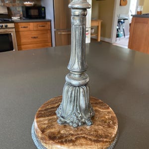 May include: A vintage lamp base with a silver-toned metal stem and a round, brown and tan marble base. The base has a decorative, ornate design and a threaded top for attaching a lamp shade.