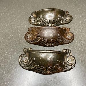 May include: Three antique metal drawer pulls with ornate, leaf-shaped designs. The pulls are a dark, aged bronze color.