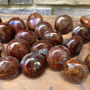 May include: A collection of round, polished door knobs featuring a marbled, swirling pattern of deep brown, amber, and reddish-tan tones. Each knob has a smooth, glossy finish with a spherical shape, and some include visible metal hardware stems.