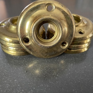 May include: A collection of vintage brass door rosettes. The rosettes are circular with a central hole and smaller screw holes. The brass has a warm, aged patina, suggesting they are antique or reclaimed hardware.