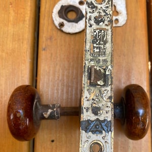 May include: Antique door hardware with ornate details, featuring a white and black painted design. The hardware includes a door knob with a brown ceramic finish and a latch with a sliding mechanism. The latch has a metal plate with the text "Yale & Towne Mfg. Co.  New York" inscribed on it.