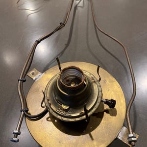 May include: A brass lamp fixture with a black knob and a label that reads "Eagle". The fixture has a metal frame and is attached to a wire.