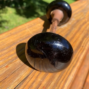 May include: A vintage door knob set featuring two smooth, glossy black spherical knobs connected by a central metal spindle. The surface of the black knobs shows minor surface scratches and a reflective finish, with a metallic rod visible between them.