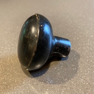 May include: A black, round door knob with a slightly raised edge around the perimeter. The knob has a small hole on the side for a screw.