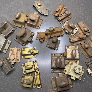 May include: A collection of vintage metal latches in various sizes and shapes. The latches are in shades of gold, silver, and brown, with signs of wear and rust. Some have knob handles, while others have lever handles.