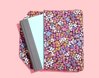 May include: A book cover with a floral pattern in shades of pink, orange, yellow, and blue on a dark purple background. The book cover is made of fabric and has a grey spine.