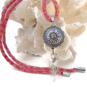 May include: A pink and white lanyard with a silver retractable badge holder featuring a decorative flower design with a clear rhinestone in the center.