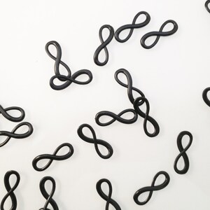 May include: A scattering of black infinity symbol charms on a white background.