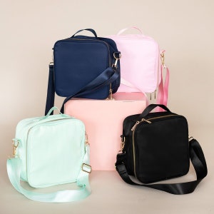 May include: Four different colored zippered makeup bags with gold hardware and adjustable straps. The bags are navy blue, light pink, light green, and black.