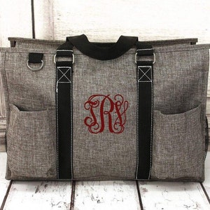 May include: A gray and black tote bag with a red monogram "JRS" embroidered on the front. The bag has two black handles and a zipper closure.