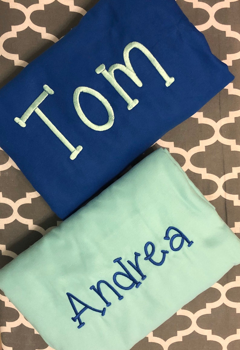 May include: Two personalized blankets, one blue with the name "Tom" embroidered in white, and one light blue with the name "Andrea" embroidered in blue.
