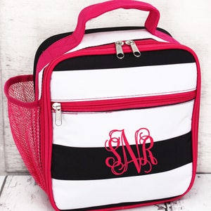 May include: A lunch bag with black and white horizontal stripes, a pink handle, and a pink zipper. The bag has a pink mesh side pocket and a pink monogram on the front. The bag is designed to carry food and drinks.
