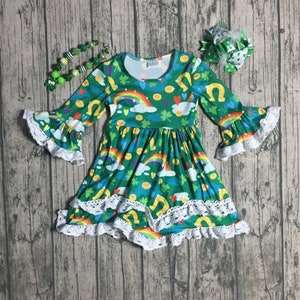 May include: A green dress with a rainbow, shamrock, and horseshoe print. The dress has a white lace trim and bell sleeves.