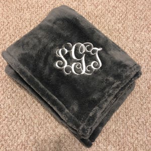 May include: A gray plush throw blanket with a white embroidered monogram of the letters "SGC".