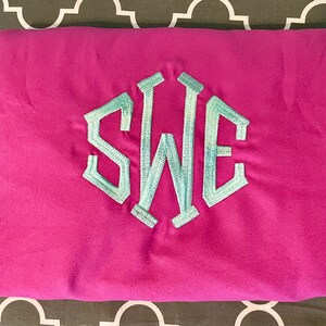 May include: A folded pink t-shirt with a light blue embroidered monogram of the letters "SWE" in a hexagonal shape.