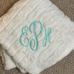 May include: White faux fur throw blanket with a light blue embroidered monogram "EPJ".