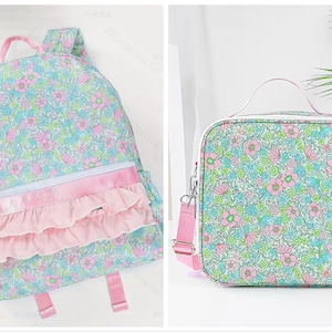 May include: A floral print backpack and matching lunch bag. The backpack has a light blue background with pink and green flowers, a pink ruffle pocket, and pink straps. The lunch bag has a similar floral pattern with a pink strap.