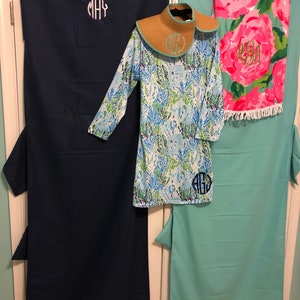 May include: Two beach towels with monogrammed initials, one in navy blue and one in turquoise, with a blue and green floral print cover-up and a straw sun hat.