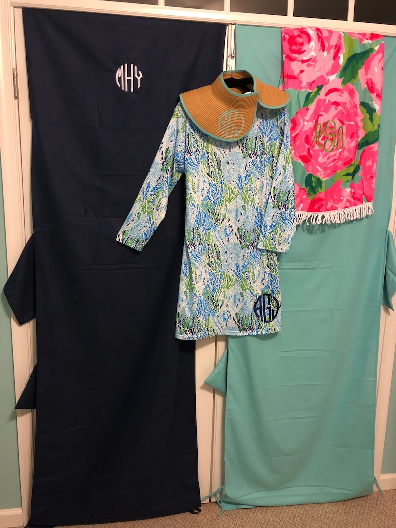 May include: Two beach towels with monogrammed initials, one in navy blue and one in turquoise, with a blue and green floral print cover-up and a straw sun hat.