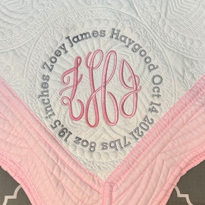May include: A white and pink baby quilt with a monogrammed circle in the center. The circle includes the name "Zoey James Haygood" and the date "Oct 14 2021". The quilt is 36 inches by 36 inches and weighs 8 oz.