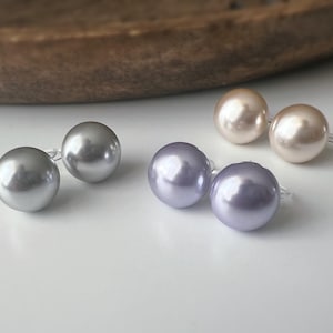 Peut inclure: Boucles d'oreilles en perles de différentes couleurs. Les boucles d'oreilles rondes ont une finition brillante. Les couleurs comprennent l'argent, le lavande et le champagne clair. Présentées sur une surface blanche.