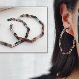 Peut inclure: Une paire de grandes boucles d'oreilles hexagonales colorées. Les boucles d'oreilles sont en plastique marbré multicolore.