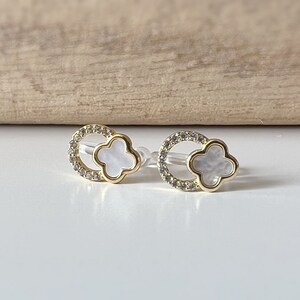 May include: A pair of gold earrings with a white clover-shaped stone set in a circle of clear rhinestones.