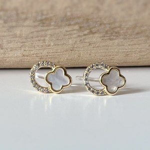 May include: A pair of gold earrings with a white clover design. The clover is surrounded by a circle of small clear stones.