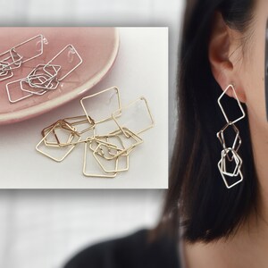 Könnte beinhalten: Ein Paar geometrische Ohrringe in Gold und Silber mit einem kettenartigen Design. Die Ohrringe bestehen aus mehreren quadratischen Formen, die miteinander verbunden sind.