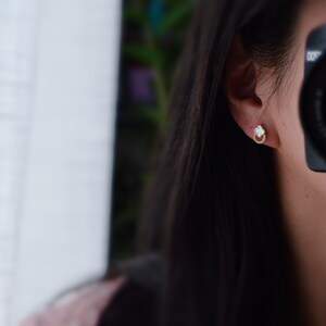 May include: A pair of gold earrings with a white stone in the center and a circle of small stones around the edge.