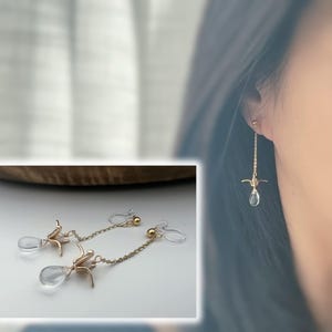 Può includere: Un paio di orecchini a clip dorati con una catena delicata e un cristallo trasparente a forma di lacrima. Gli orecchini presentano un piccolo design a forma di uccello.