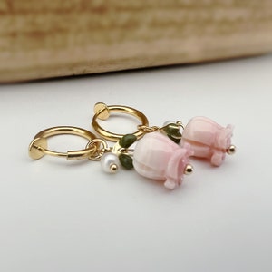 Peut inclure: Boucles d'oreilles créoles dorées avec un charme de fleur rose et des accents de feuilles vertes. Le charme de la fleur a une perle suspendue.