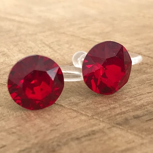 Puede incluir: Un par de pendientes de clip de cristal rojo. Los pendientes son redondos y tienen un diseño facetado. Están montados en un clip de plástico transparente.